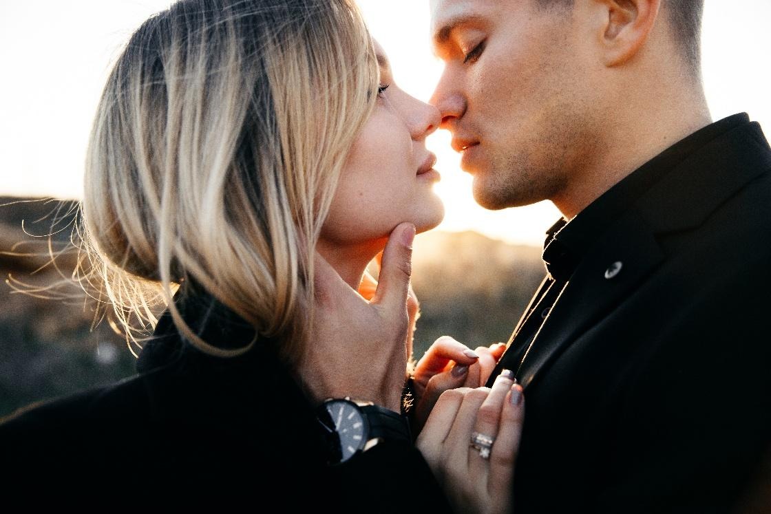 Side view close-up of a young couple with full lips and smooth skin kissing on Valentine’s Day against a glowing sunset sky.